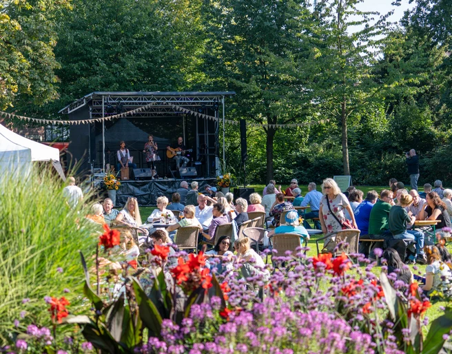 Spätsommerkonzert Open-Air-Konzert im Grünen mit Musikern auf Bühne und Publikum an Tischen im Sonnenschein.