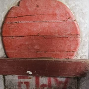 Sonderausstellung Jungbluth1.jpg Roter, runder Stein mit horizontalen Linien, montiert auf einer unregelmäßigen, hellen Wand.