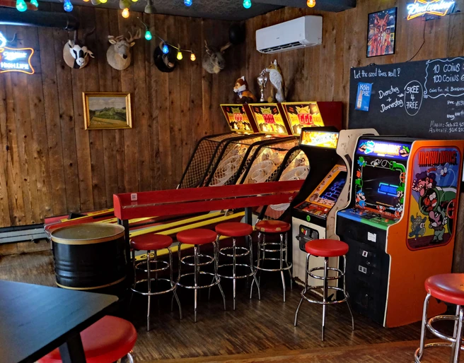 Skeeball and arcade games in the Red Fox Bar Eine rustikale Bar mit Holzwänden, Arcade-Spielen, roten Barhockern und entspannter Atmosphäre.A rustic bar with wooden walls, arcade games, red bar stools and a relaxed atmosphere.