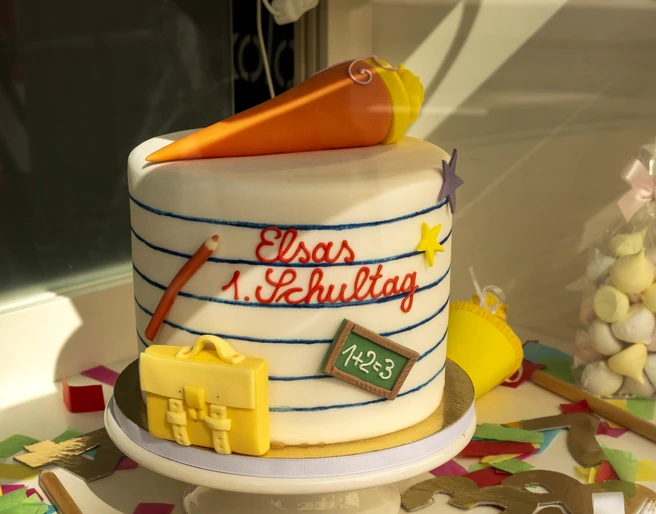 Madame Miammiam Bunter Einschulungskuchen mit Tafel, Schultüte und Schokolade als Verzierung auf einer Tortenplatte.Colorful first school cake with blackboard, school cone and chocolate as decoration on a cake plate.