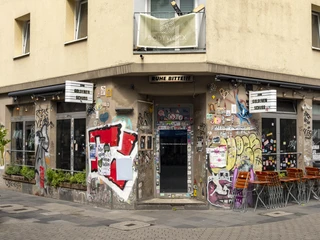 Zum Goldenen Schuss Eingang der Kneipe voll von bunten Graffiti, mit mehreren Tischen im Freien.Entrance of the pub full of colorful graffiti, with several tables outside.