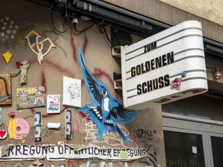 Zum Goldenen Schuss Bunte Street-Art mit Vogelmotiv und Graffiti an einer Hauswand im urbanen Köln.Colorful street art with a bird motif and graffiti on a house wall in urban Cologne.