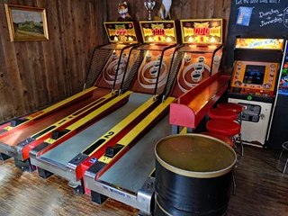 Skeeball lanes in the Red Fox Bar Zwei Skee-Ball-Automaten stehen in einer Holzwand-Nische, daneben ein Donkey Kong Arcade Game.Two Skee-Ball machines stand in a wooden wall niche, next to a Donkey Kong arcade game.