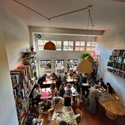 Bingo Club Cologne Ein lebendiger Raum voller Menschen, die an verschiedenen Tischen Brettspiele spielen, mit Regalen voller Spiele an den Wänden.A lively room full of people playing board games at various tables, with shelves full of games on the walls.