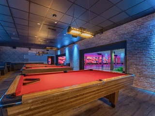 Billiard tables at West Bowling Ein moderner Billardraum mit drei leuchtend roten Tischen, umgeben von gemauerten Wänden und stimmungsvollem Licht.A modern billiard room with three bright red tables, surrounded by brick walls and atmospheric lighting.