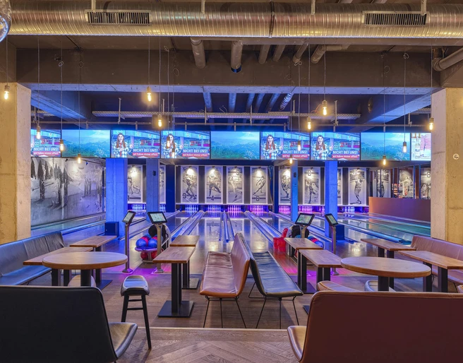 Bowling lanes at Underlux Interieur des Underlux Bowlingcenters mit blauen und violetten Lichtern, Tische im Vordergrund.Interior of the Underlux bowling center with blue and purple lights, tables in the foreground.