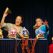 Knallwut Zwei Puppenspielerinnen animieren bunte, fantasievolle Puppen auf einer kleinen Bühne mit Vorhang.