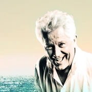 Alexis Sorbas Porträt eines lächelnden älteren Mannes vor einem weiten, sanft beleuchteten Ozean bei Sonnenuntergang.