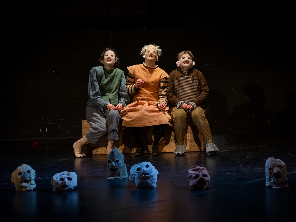 Schauspiel Leipzig spielt Hamlet Frei nach William Shakespeare Drei Darsteller mit ausdrucksstarken Masken sitzen auf der Bühne, von Totenkopfmasken umgeben.