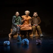 Schauspiel Leipzig spielt Hamlet Frei nach William Shakespeare Drei Darsteller mit ausdrucksstarken Masken sitzen auf der Bühne, von Totenkopfmasken umgeben.