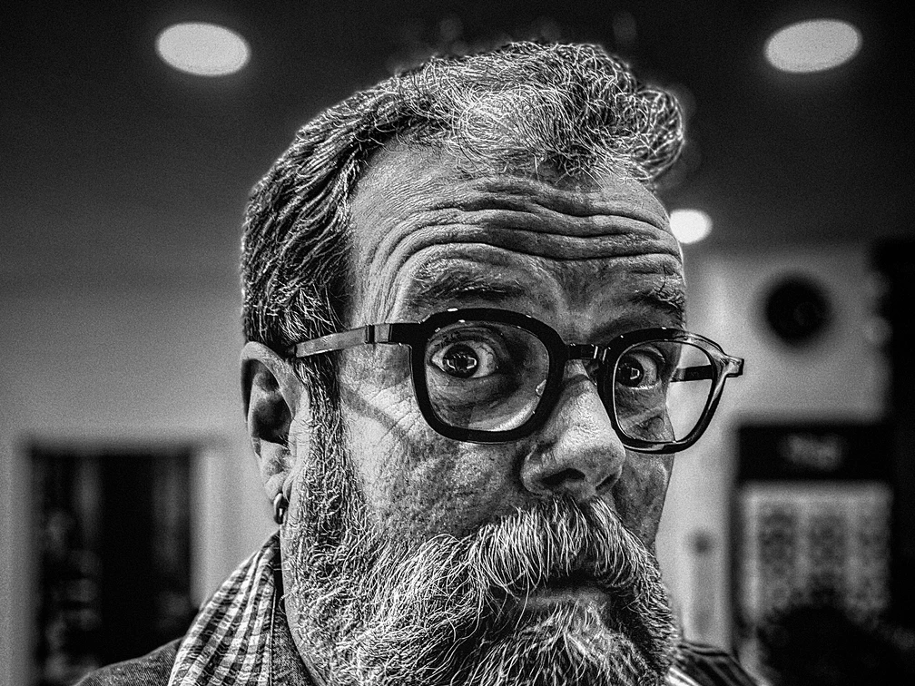 Jochen Malmsheimer Schwarz-Weiß-Porträt von Jochen Malmsheimer mit Bart und Brille, der intensiv in die Kamera schaut.