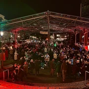 Erkrather Feierabendmarkt - Christmas Edition Menschenmenge versammelt sich abends bei festlicher Beleuchtung unter einer großen Markthalle.