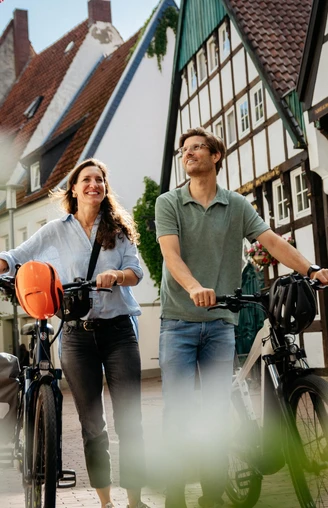 Unterwegs in der Altstadt von Osnabrück  Zwei Personen laufen mit Fahrrädern durch eine gepflasterte Straße mit Fachwerkhäusern.