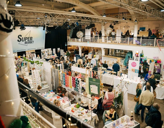 The Super Christmas Market Blick auf einen belebten Weihnachtsmarkt zur Adventszeit, wo zahlreiche Besuchende an bunten Ständen stöbern.View of a lively Christmas market during the Advent season, where numerous visitors browse the colorful stalls.
