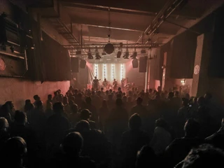 Gebäude 9 Das Bild zeigt eine gut besuchte Konzertveranstaltung in einem düsteren Raum mit stimmungsvoller Beleuchtung.The picture shows a well-attended concert event in a gloomy room with atmospheric lighting.