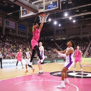 Telekom Baskets Bonn Spieler in pinken Trikots dominieren ein Basketballspiel in einer großen, voll besetzten Arena.Players in pink jerseys dominate a basketball game in a large, packed arena.