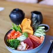pexels-valeriya-20571427.jpg Bunter Poké Bowl mit frischem Lachs, Thunfisch, Edamame, Garnelen und Gemüse auf einem Holztisch.