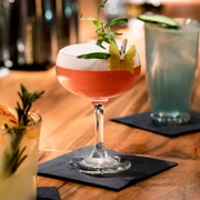 Suderman Ein Cocktailglas mit roter Flüssigkeit und Schaumkrone steht auf einem Holztresen.A cocktail glass with red liquid and a head of foam stands on a wooden counter.