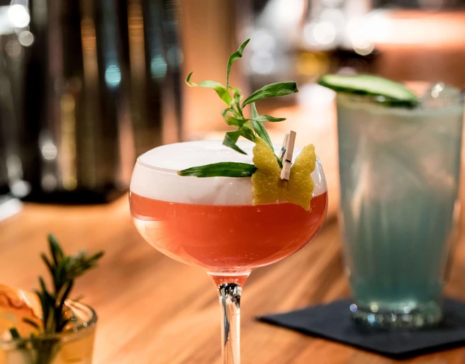 Suderman Ein Cocktailglas mit roter Flüssigkeit und Schaumkrone steht auf einem Holztresen.A cocktail glass with red liquid and a head of foam stands on a wooden counter.