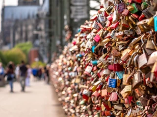 Love locks in Cologne Eine Vielzahl von bunten Liebesschlössern ziert das Geländer der Hohenzollernbrücke in Köln. Im Hintergrund verschwimmt die Silhouette des majestätischen Kölner Doms, ergänzt durch die vorbeiziehenden Menschen auf der Brücke, die zu Fuß den Rhein überqueren.A multitude of colorful love locks adorn the railing of the Hohenzollern Bridge in Cologne. The silhouette of the majestic Cologne Cathedral blurs in the background, complemented by the people passing by on the bridge as they cross the Rhine on foot.