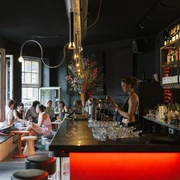OFF Bar Eine bunt beleuchtete Bar mit Gästen, die an Tischen plaudern und Drinks genießen.A colorfully lit bar with guests chatting at tables and enjoying drinks.