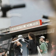 Der klitzekleine Weinladen Vor einem kleinen Geschäft in der Stadt versammeln sich Menschen. Fahrräder sind im Vordergrund.People gather in front of a small store in the city. Bicycles are in the foreground.