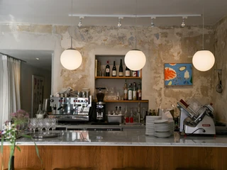Frohnatur Bistrooo & Bar Bar Bar Drei kugelförmige Hängelampen leuchten über einer Theke mit Weingläsern, Kaffeemaschine und Brotschneidemaschine.Three spherical hanging lamps light up above a counter with wine glasses, a coffee machine and a bread slicer.