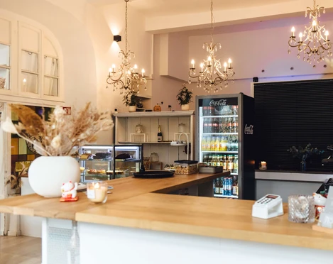 Das Neandertal No. 1 - Café und Events in Erkrath Ein helles Café mit Kronleuchtern, Holztresen und Kühlvitrinen, das eine warme Atmosphäre ausstrahlt.