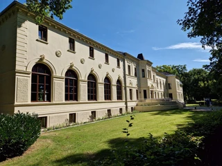 Altes-Kurhaus-Front.jpg Die Fassade des historischen Alten Kurhauses in Bad Zwischenahn unter klarem, blauem Himmel.