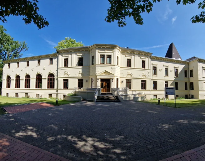 Altes-Kurhaus-Panorama.jpg Altes Kurhaus mit großen Fenstern, umgeben von Bäumen, in Bad Zwischenahn unter blauem Himmel.