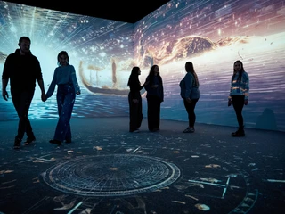 Tutankhamun - His Tomb and His Treasures Eine Gruppe von Menschen bewegt sich in einem dunklen Raum, umgeben von ägyptischen Lichtprojektionen.A group of people move around in a dark room, surrounded by Egyptian light projections.