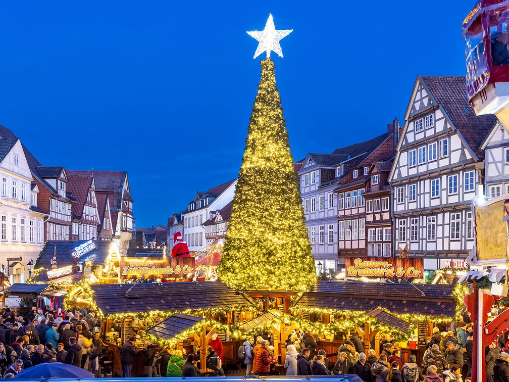 Weihnachtsmarkt Celle  Weihnachtsmarkt in Celle: Leuchtender Tannenbaum, umgeben von Fachwerkhäusern und Menschenmenge.