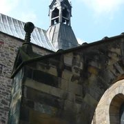 6 Stiftskirche.JPG Glockenturm der Stiftskirche mit steinernem Bogen und mittelalterlichem Mauerwerk unter blauem Himmel.