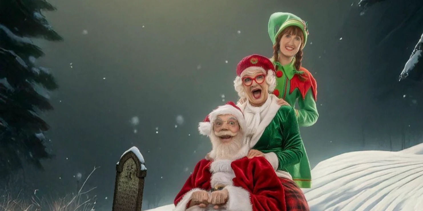 Mord am Nordpol_Schlitten.jpeg Zwei lachende Personen im Weihnachtskostüm sitzen auf einem verschneiten Hügel vor dunklem Hintergrund.