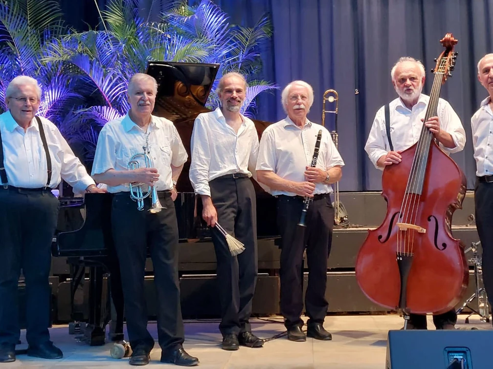 Bandfoto Swinging Oldtimers (1).jpg Sechs Musiker der Swinging Oldtimers stehen mit Instrumenten grinsend in eleganter Kleidung auf der Bühne.