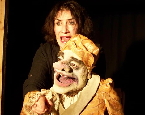 ambrella-figurentheater-der-eingebildete-kranke-1.jpg Frau spielt mit lebendiger Puppe in goldener Kleidung eine Theaterszene voller Ausdruckskraft.