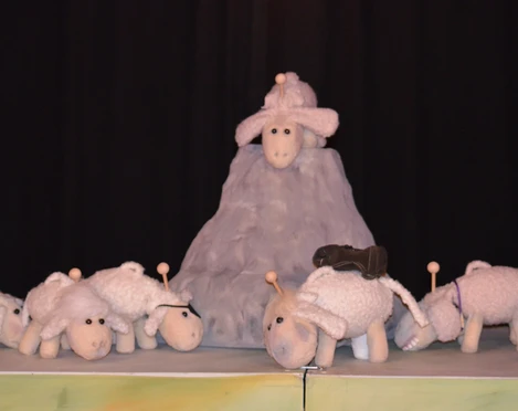 figurentheater-grinsekatze-das-letzte-schaf-2.jpg Mehrere weiße Schafpuppen stehen auf einer Bühne, eines thront erhöht auf einem grauen Hügel.