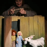 ambrella-figurentheater-zottelhaube-1.jpg Puppenspielerin lenkt Marionetten von zwei Kindern und einer Ziege in einer Holzkulisse.