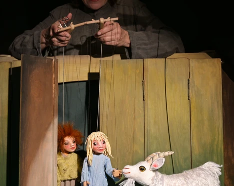 ambrella-figurentheater-zottelhaube-1.jpg Puppenspielerin lenkt Marionetten von zwei Kindern und einer Ziege in einer Holzkulisse.