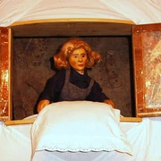 figurentheater-ernst-heiter-frau-holle.jpg Holzfigur der Frau Holle steht am Fenster und schüttelt ein weiß besticktes Kissen aus.