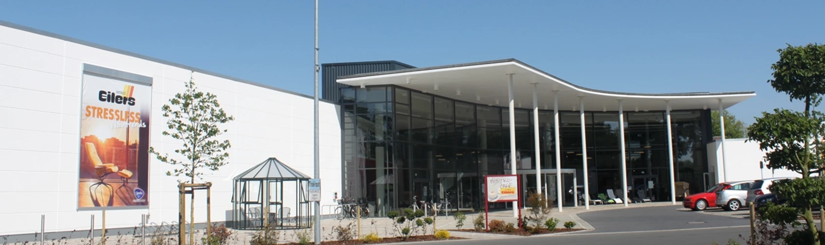 Möbel Eilers  Eingangsbereich eines grossen Möbelhauses mit Sitzgelegenheit. Rechts ist ein Teil des Parkplatzes zu sehen.