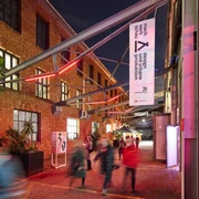 MACHWERKHAUS Belebtes Kunstzentrum bei Nacht mit roten Backsteinwänden, Menschen treten durch Eingang.Lively art center at night with red brick walls, people enter through the entrance.