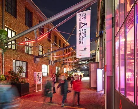 MACHWERKHAUS Belebtes Kunstzentrum bei Nacht mit roten Backsteinwänden, Menschen treten durch Eingang.Lively art center at night with red brick walls, people enter through the entrance.