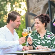 Café Ruhrnatur, Mülheim an der Ruhr Ein Paar hebt die Gläser in einem Café bei sommerlichem Abendlicht, umgeben von Natur.