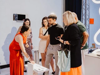 Menschen in einem Gespräch bei einer Kunstmesse; lächelnde Teilnehmer*innen in stilvoller Kleidung.People in conversation at an art fair; smiling participants in stylish clothing.