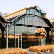 Design Post Modernes Gebäude mit Glasfassade, gewölbten Strukturen und trockenem Gras im Vordergrund.Modern building with glass façade, arched structures and dry grass in the foreground.