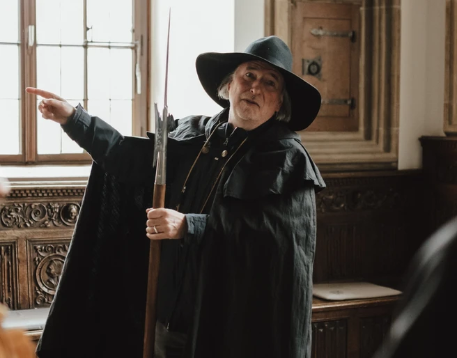 Nachtwächter (Hauptbild).jpg Ein Nachtwächter im historischen Kostüm erklärt Besuchern in einem traditionell eingerichteten Raum Details.A night watchman in historical costume explains details to visitors in a traditionally furnished room.Een nachtwaker in historisch kostuum geeft uitleg aan bezoekers in een traditioneel ingerichte kamer.