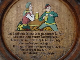 Beschwipster Nachtwächter (3).jpg Holzteller mit gemalten Nachtwächtern im Mittelalter, die Bier an einem rustikalen Tisch genießen.
