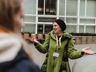 Altstadt-Highlights (3).jpg Ältere Frau in grünem Mantel, gestikuliert lächelnd, vor moderner Glasarchitektur im Hintergrund.Older woman in a green coat, gesticulating and smiling, in front of modern glass architecture in the background.Oudere vrouw in groene jas, gebarend en glimlachend, voor moderne glazen architectuur op de achtergrond.
