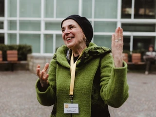 Altstadt-Highlights (2).jpg Ältere Frau in grünem Mantel und schwarzer Mütze lacht herzlich auf einem städtischen Platz.Elderly woman in a green coat and black cap laughs heartily in a city square.Oudere vrouw in groene jas en zwarte pet lacht hartelijk op een stadsplein.